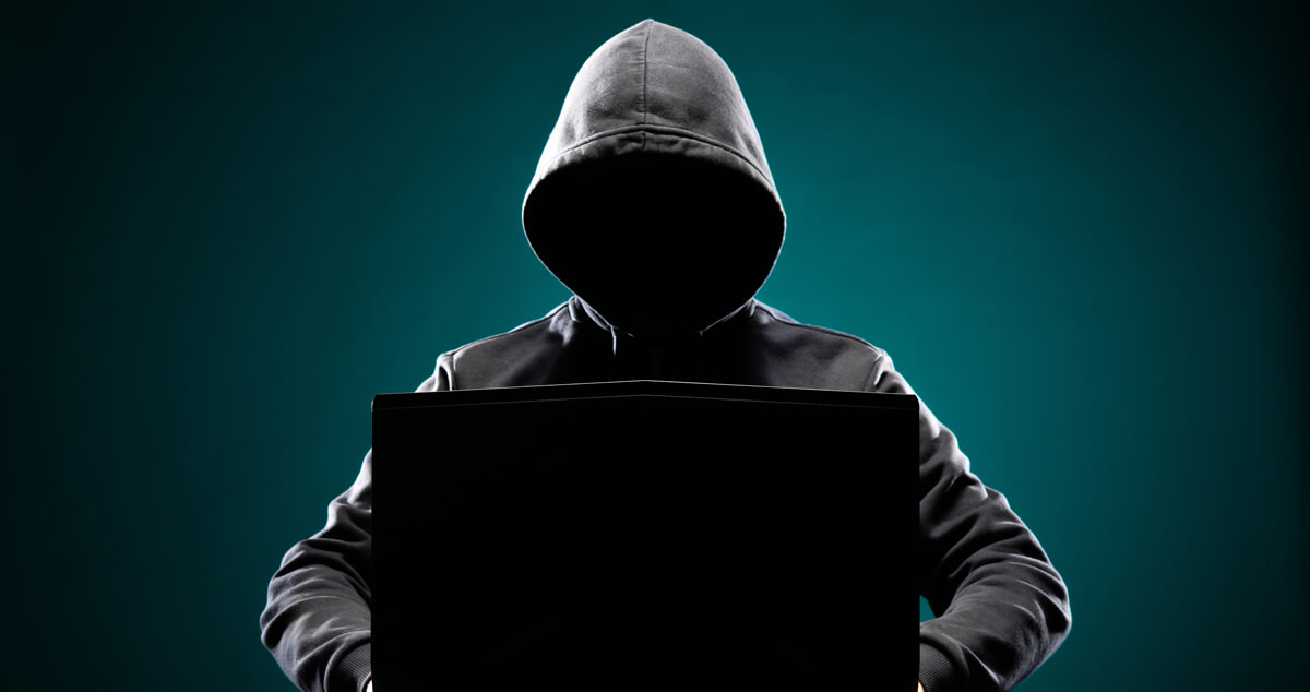 Man sitting in the shadows behind a computer depicting an identity thief