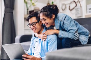 a couple on their couch at home looking at the costs of refinancing online