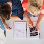 an overhead shot of a couple with a calculator and paperwork for refinancing their mortgage